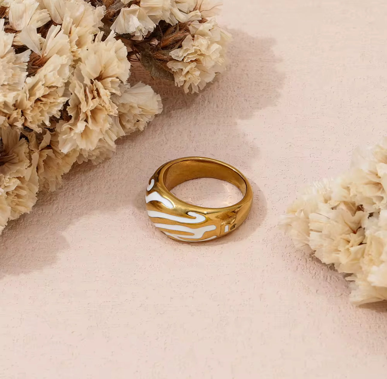 Gold ring with white marbled design on a pink surface with beige flowers