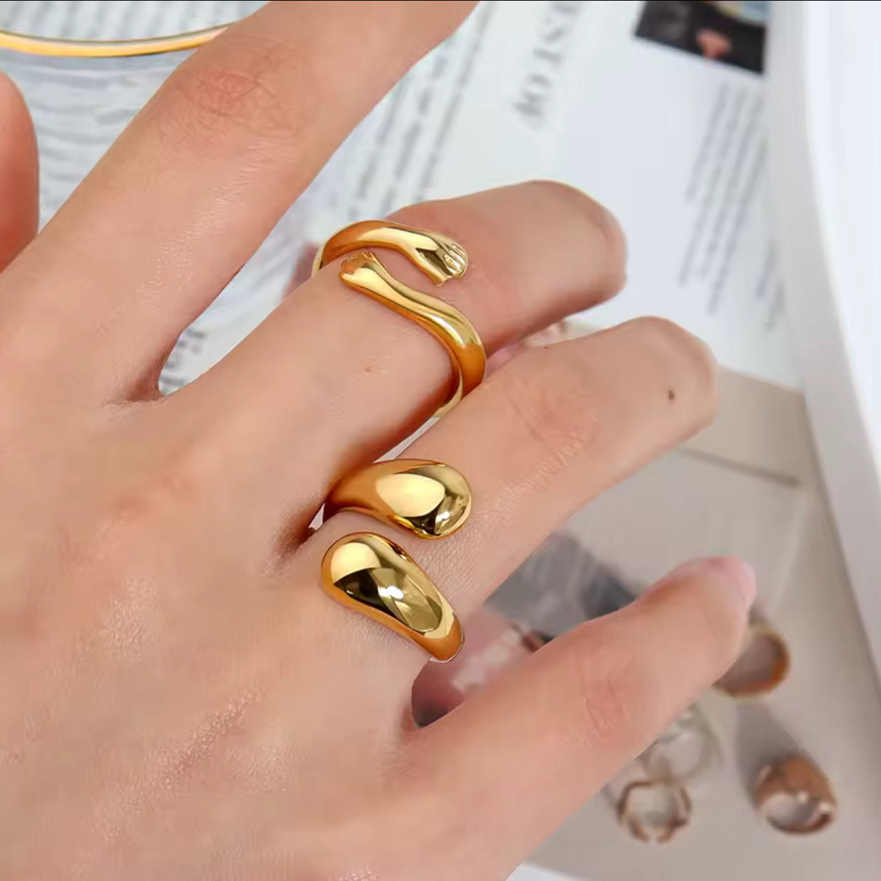 Model wearing the Embrace Ring stacked with other rings, showing the two-hands open design