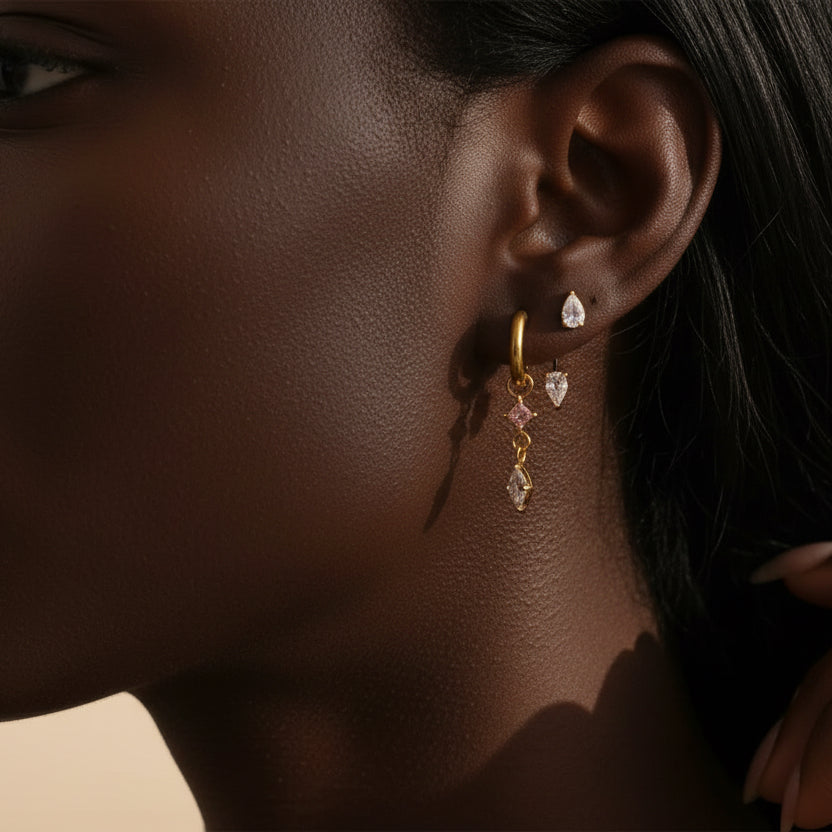 Close-up of an ear wearing a gold earring with dangling crystals.