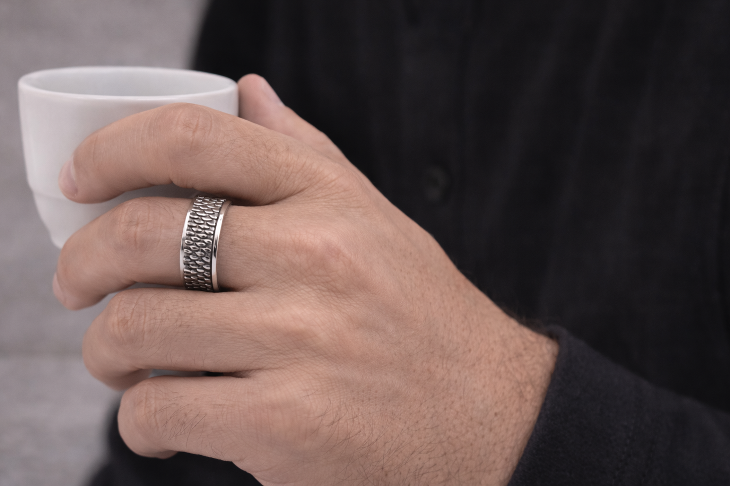 Hand wearing a silver ring holding a white cup against a blurred background