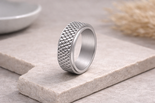 Silver ring with textured design on a light stone surface