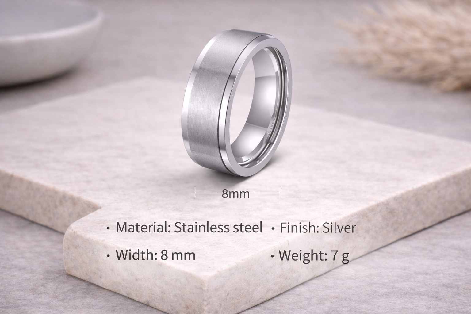 Silver ring on a stone surface with material and size details.
