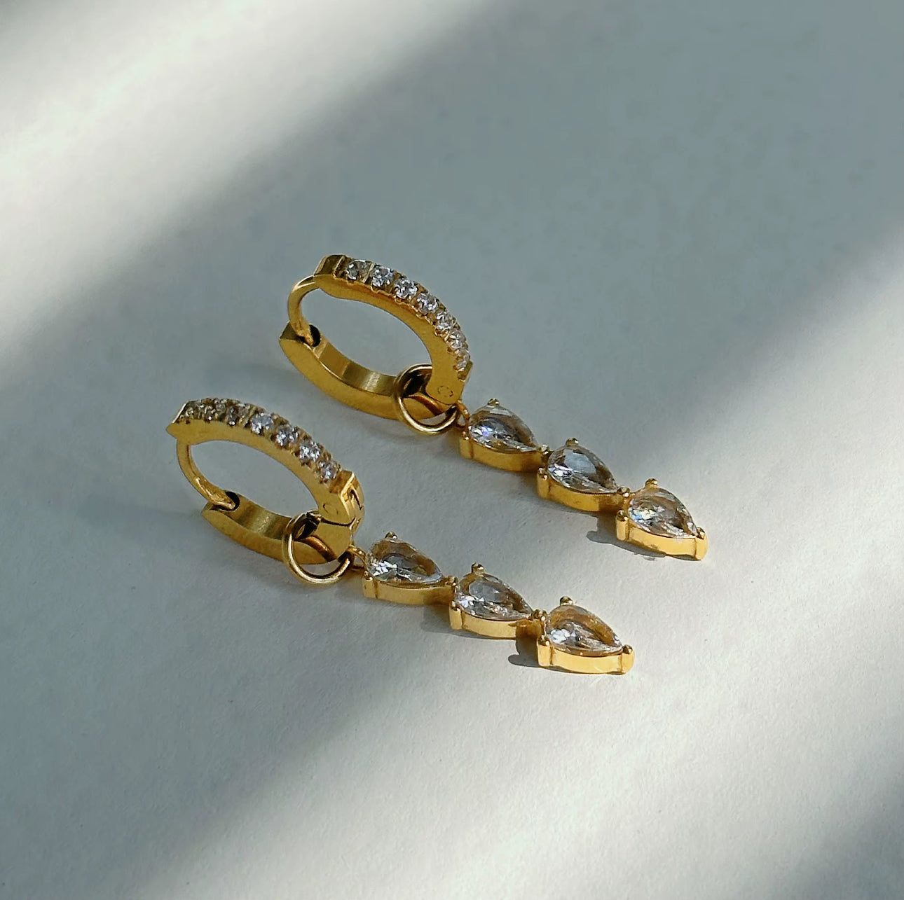 Gold earrings with clear gemstones on a light gray background