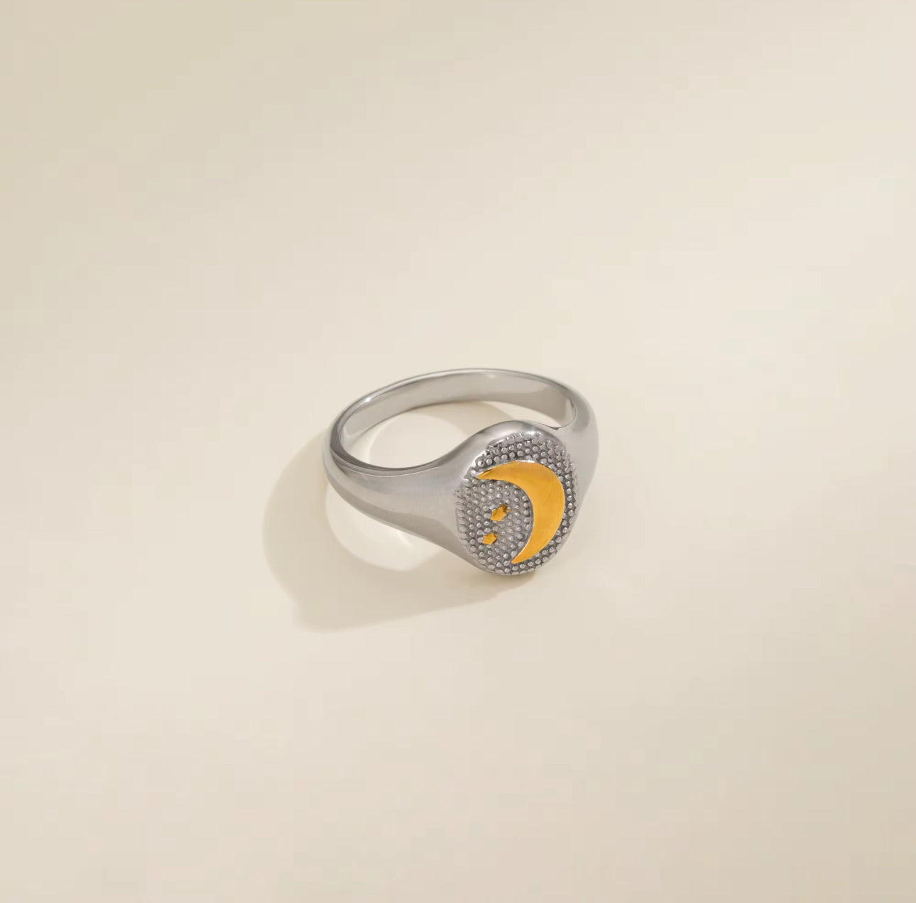 Silver ring with a yellow crescent moon design on a beige background