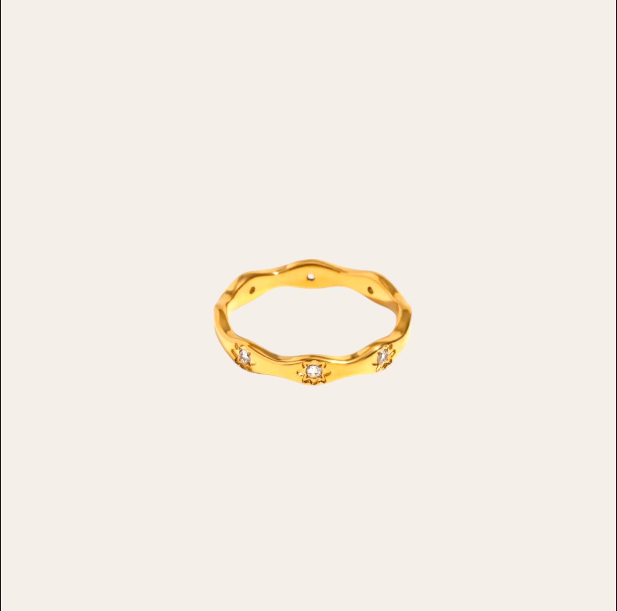 Astro Ring, wavy gold-plated band with starburst-set clear zircon on plain background