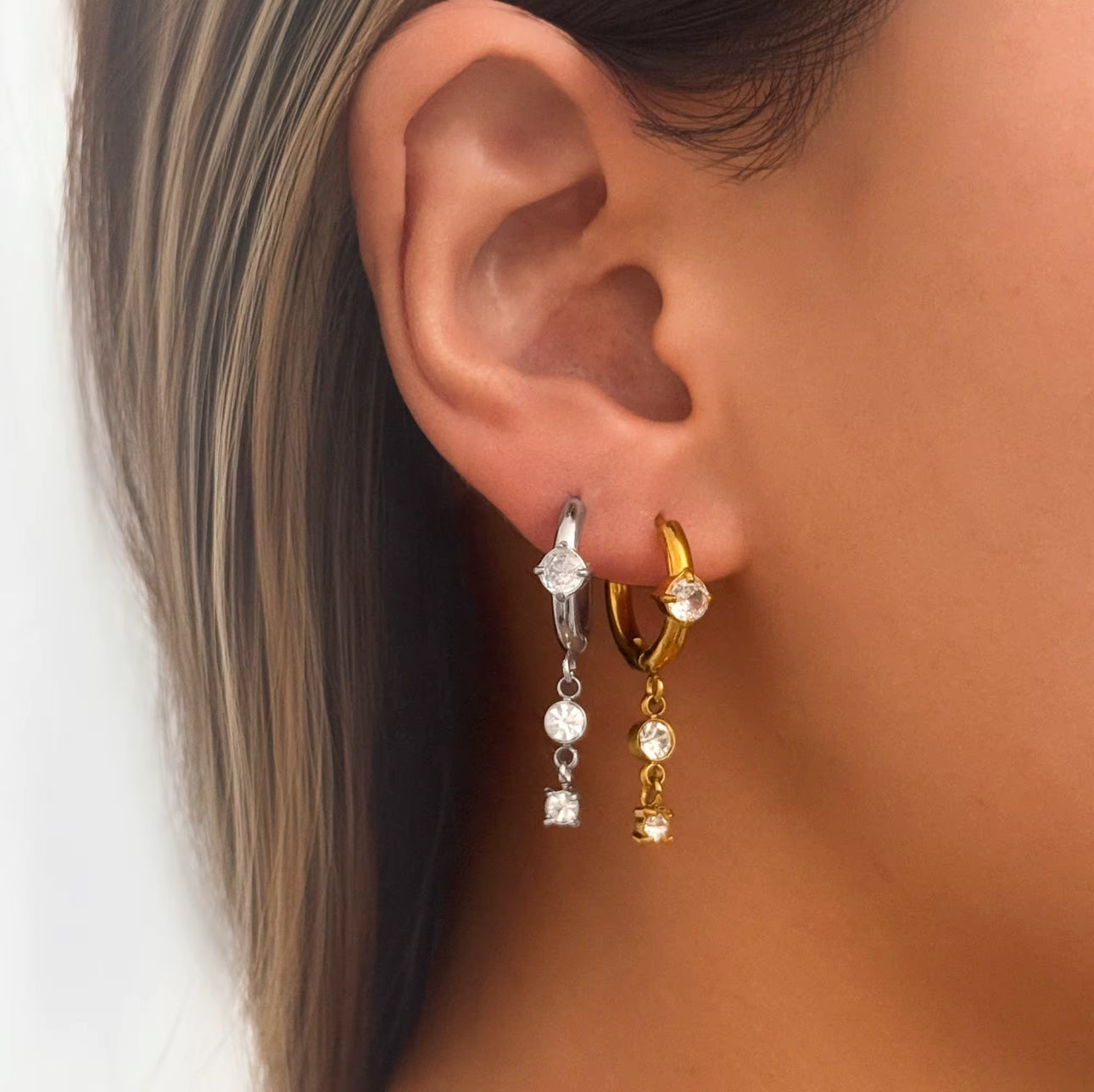 Silver aura drop hoop earrings worn on ear with clear zircon stones