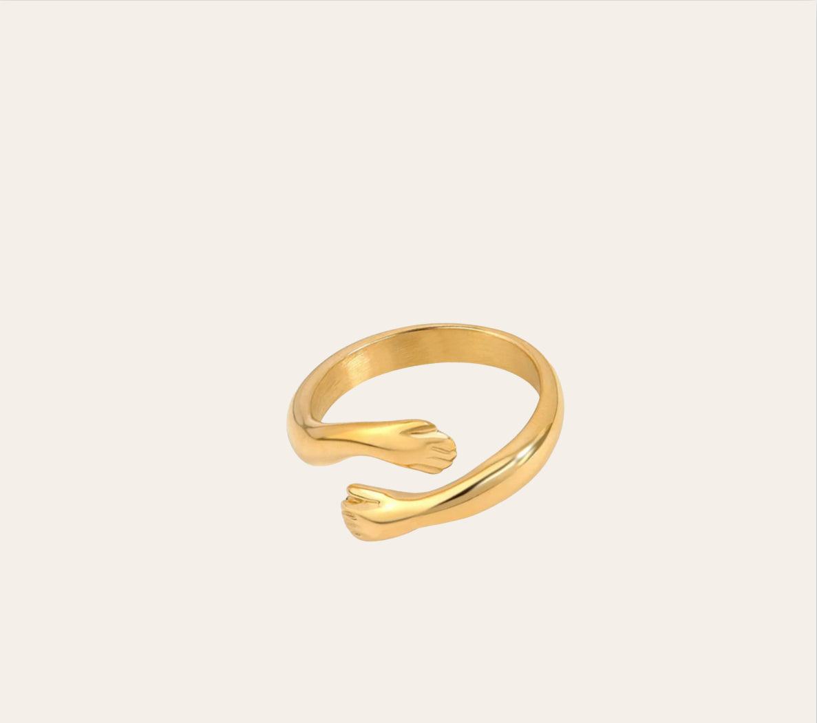 Embrace Ring—open-ended band with two small hands in 18k gold-plated 316L stainless steel on plain background