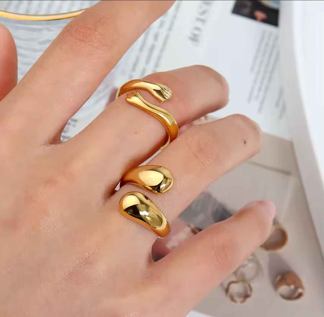 Model wearing the Embrace Ring stacked with other rings, showing the two-hands open design