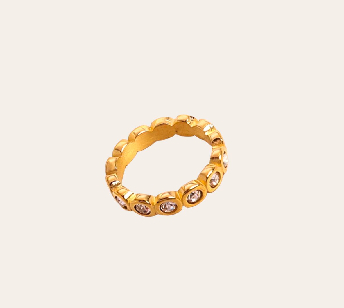 ady Ring, gold-plated scalloped bezel eternity band with clear zircon stones on plain background