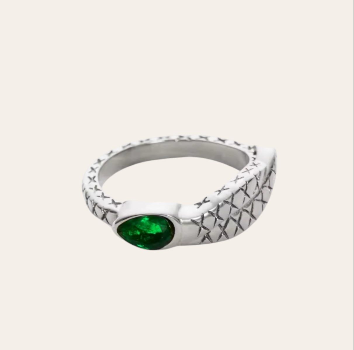 Snake Ring in polished stainless steel with green zircon on plain background.